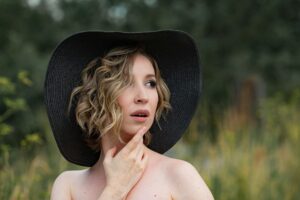 young attractive girl in black hat fedora in tall grass in a field